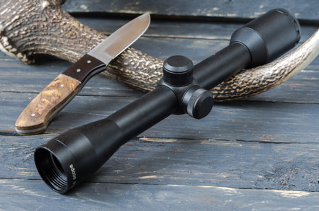 Optical sight and hunting knife. Dark wooden background.