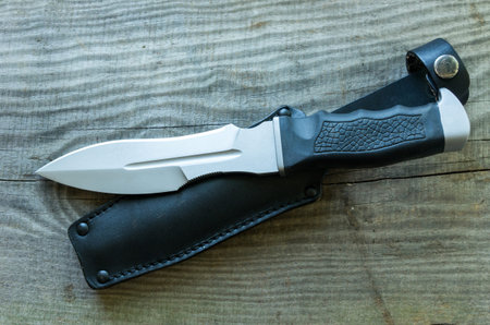 Army knife and black leather case. Wooden background. A dangerous knife.