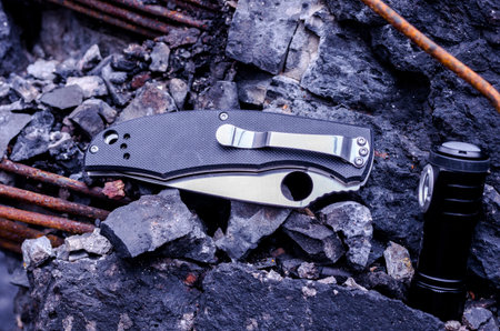 The knife is folded. Headlamp. Knives and a flashlight on the background of debris. Black object on...