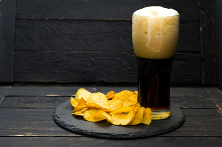 A glass of dark beer and chips. Beer Foam. Beer and chips on a tray.の写真素材