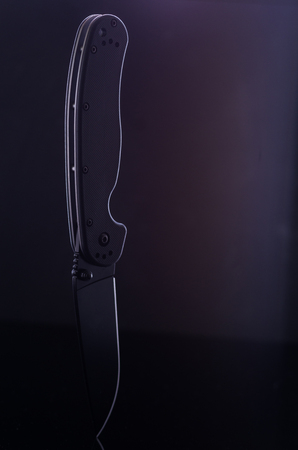 Big black knife on a black background. Folding black knife. Vertical frame.の写真素材