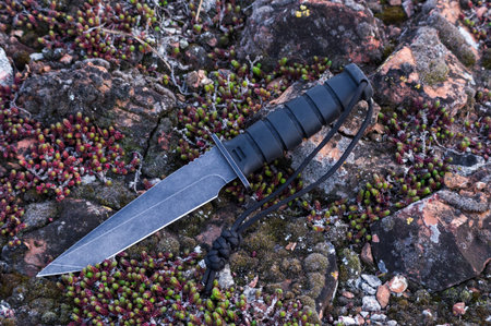 Large army knife on the moss. Big black knife.