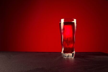 A glass of red drink. Glass of drink on a red background. Foreground.の写真素材