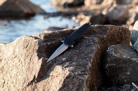 Knife on a background of stone and river. Knife dagger on the stone. Large granite stone.