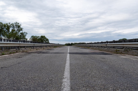 Asphalt road on the bridge. Asphalt road with patches. Leading road with a strip. Horizon and clouds.の写真素材