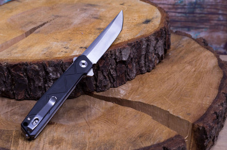 Folding knife on wooden slices. Knife and alder tree. Pocket knife with a clip. Knife diagonally...