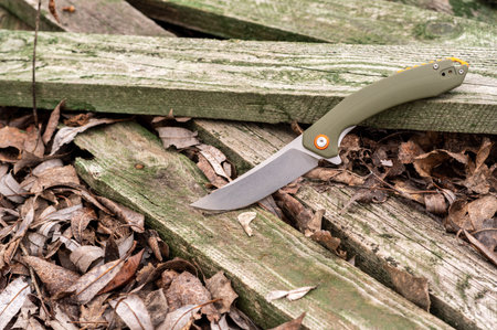 Knife with a green handle on green wooden boards. Photo of a knife in the forest. Top.