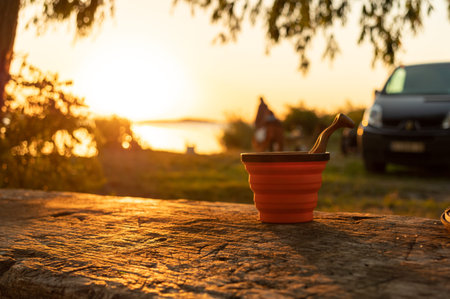 A glass and a spoon on the table. A silicone mug and a wooden spoon on the table during sunrise....