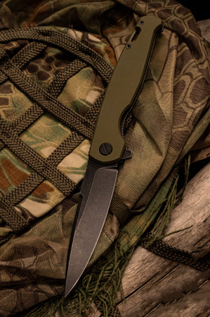 A knife lying on a military uniform. Knife and camouflage clothing. Disguise. Vertical frame.