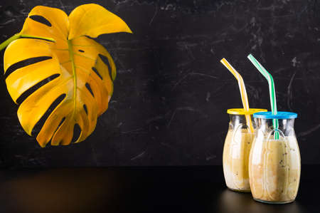 Two glasses with a cocktail. Cocktails with a straw on a black background. Monstera in the background.の写真素材
