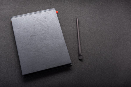 Black notebook on a black table. Black notebook and pen on the table.