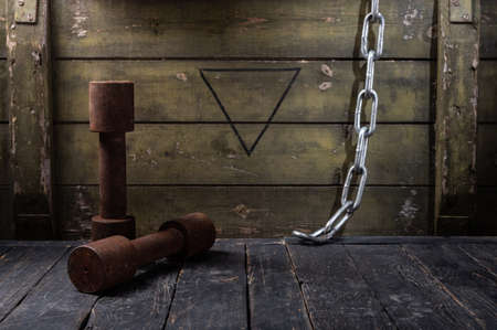 Old rusty dumbbells and chain. Dark room with dumbbells. Front view.の写真素材