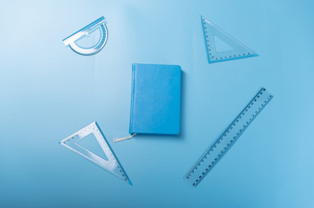 A variety of rulers and a notebook. Blue rulers and blue notepad on a blue background.