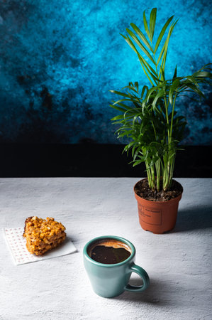 A mug of coffee and a cake. A pot with a plant on the table. Vertical frame.