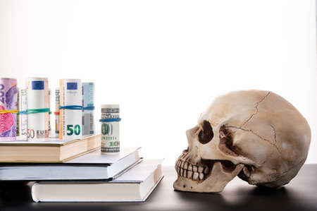 Money on the steps. Money on books. Money of different currencies and a skull.の写真素材
