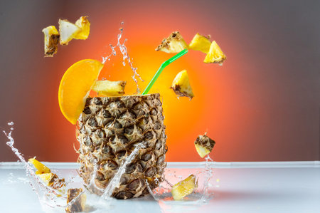 Pineapple cocktail. Pineapple with a straw. Flying pineapple slices and splashes. Citrus cocktail.