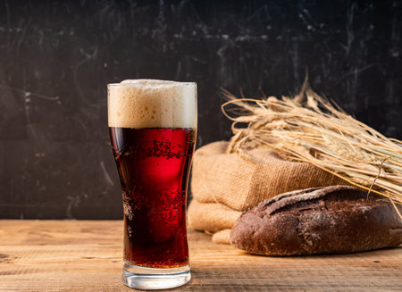 A glass of dark beer. Beer, wheat and dark bread. Dark beer and bread on a wooden table. A glass of...