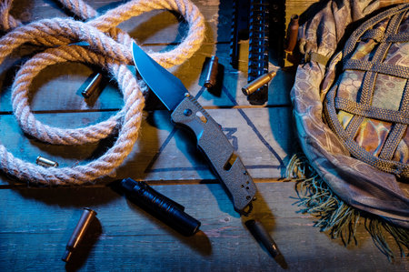 Military composition with a knife and a rope. Rope and sleeves on a military box. Warm yellow light. Knife and flashlight pocket. View from above.の写真素材