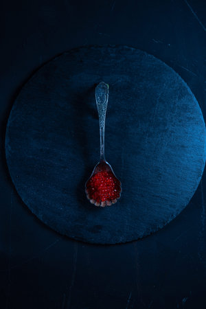 Silver spoon with red caviar. Screen on a slate pallet. Black and red. View from above.の写真素材