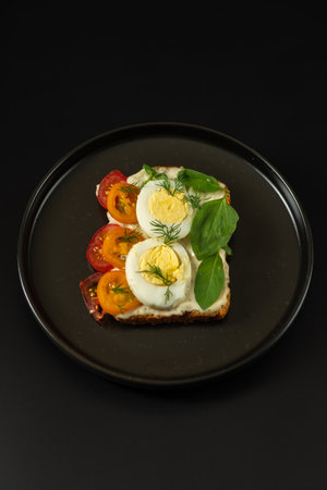 Sandwich with boiled egg and tomatoes. Sandwich on a plate. Black plate and dark background.の写真素材