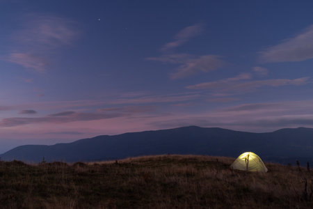 Glowing tourist tent on the top of the mountain. Sunset and tourist tent. Beautiful sunset sky and tent.の写真素材