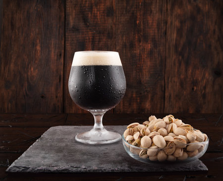 A glass of dark beer stout. Dark beer and pistachios. Serving beer and snacks. Wooden background.の写真素材