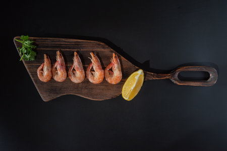 Boiled shrimps on a cutting board. Serving shrimps with lemon and herbs. Red shrimps on a black background.の写真素材