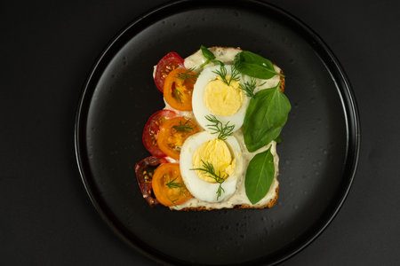 Diet sandwich on a black plate. Sandwich with boiled eggs, tomatoes and greens. Contrast of colors.の写真素材