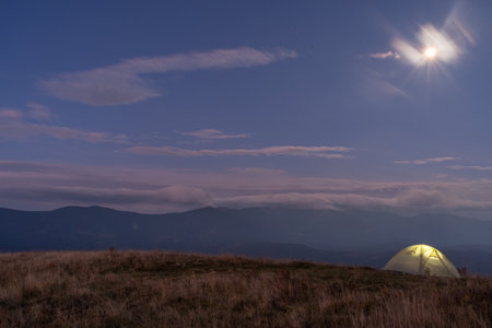 Beautiful mountain landscape. Tourist tent against the backdrop of mountains. Light in the tent that stands on the top of the mountain.の写真素材