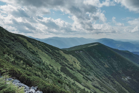 Mountain landscape with hiking trail on the ridge. Cloudy sky with cumulus clouds. Scenic view of mountain peaks, perfect for travel, trekking, and outdoor nature themes.の写真素材