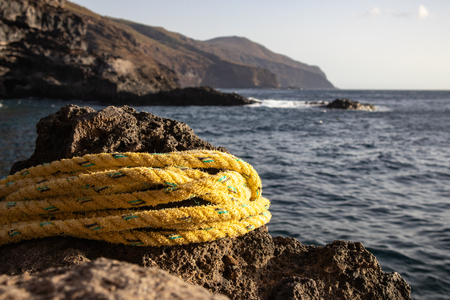 Yellow rope, wound on a rock against the background of rocks and oceanの写真素材