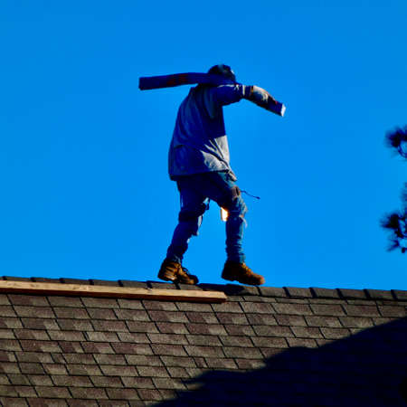 Workman carrying shingles on rooftopの写真素材
