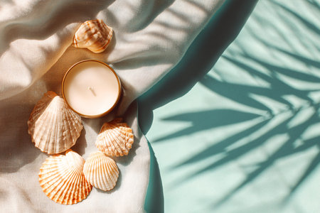 Candle and seashells on blue background with shadows from palm leaves. Flat lay, top viewの素材