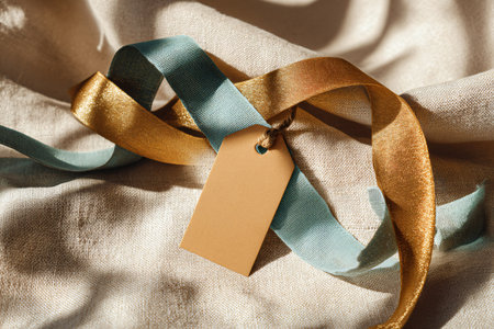 Blank tag with ribbons on light fabric background, closeupの素材