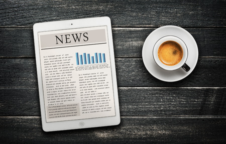 News article on digital tablet and coffee cup -black wooden 