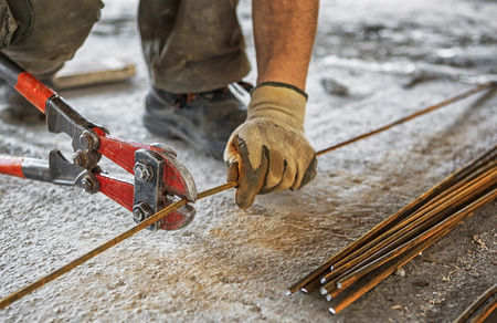 Worker cuts steel bars with bolt cutter on construction site
