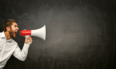 Angry young man shouting megaphone on grunge backgroundの写真素材