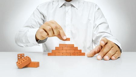 Concept of building and construction, hand put the last brick on the wall -Businessman hand placing a brick on a wallの写真素材