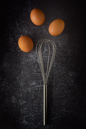 Top view three eggs and egg whisk on grunge background, preparing preparing for cooking food or dessertの写真素材