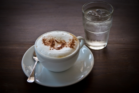 Cappuccino in white cup and a glass of water on a wooden table.の写真素材
