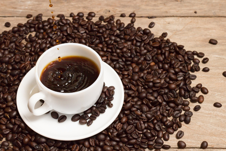pouring coffee with rosted coffee beans in white cup on a wooden background.の写真素材