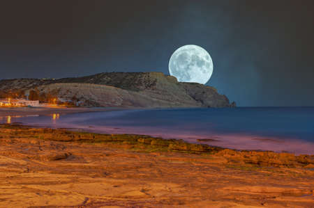 Full moon over the rocky coast of Praia da Luz in the Algarve in Portugalの写真素材