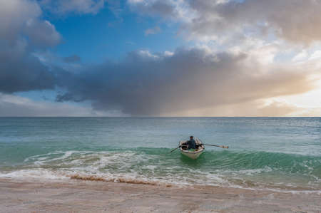 Burgau, Portugal - March 31, 2018: Fisherman rows ashore with his boat in an evening mood