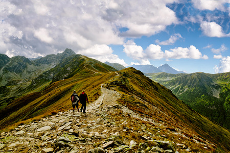 Two Man Hiking Up Steep Hill with Backpacks and Rocky Mountain Viewの写真素材