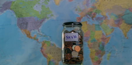 Travel budget concept. Money saved for vacation in glass jar on world map background, copy space. coins for big adventure.の写真素材