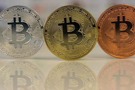 Close up of Bitcoins, gold bitcoin, silver bitcoin and bronze bitcoin with blurred background of world flags. reflection of the bitcoins visible.の写真素材