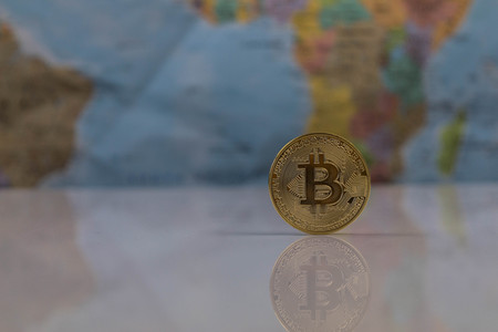Golden Bitcoin Coin close up with blurred background of world map . reflection of the bitcoin visible.の写真素材