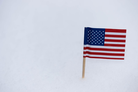 Small United State of America flag made from paper with brown toothpick on white snow background.の写真素材
