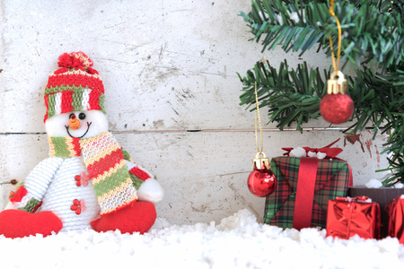 snowman sitting on the snow with christmas tree already decorated in vintage backgroundの写真素材