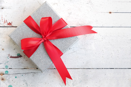 silver gift box with shiny red satin ribbon bow on vintage backgroundの写真素材
